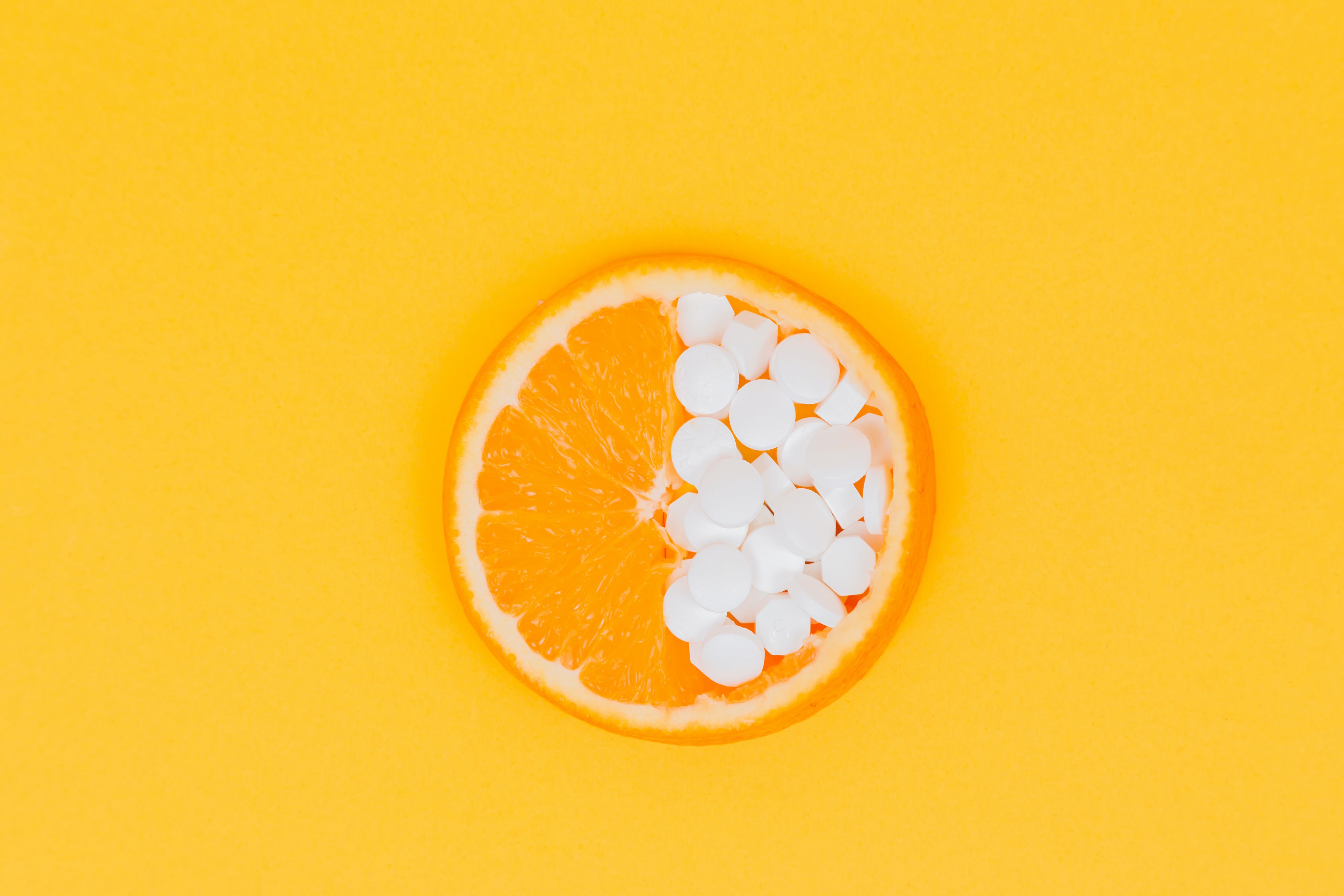 Orange slice with pills on yellow background